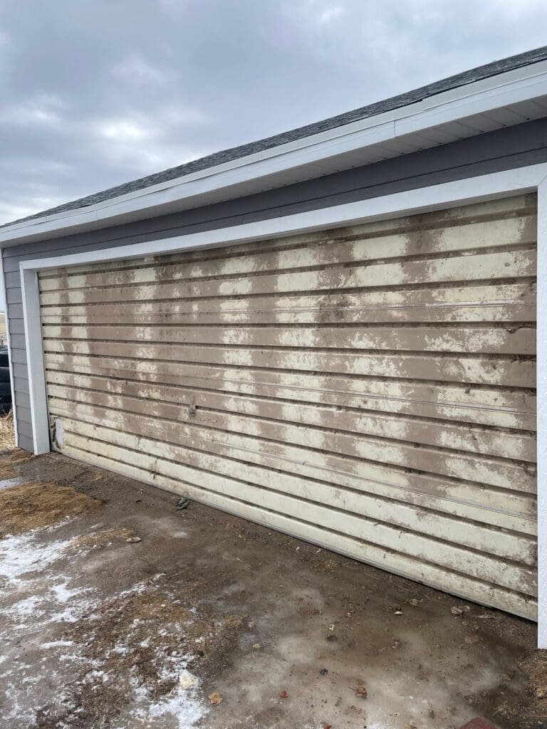Broken and dirty white residential roll-up garage door before installation by Overhead Door Company of Rapid City.