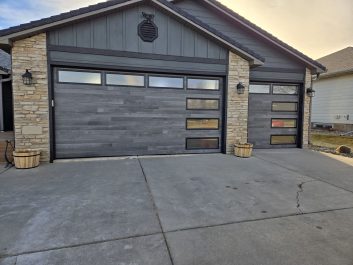 New, modern garage doors with a gray wood plank look and horizontal windows along the top and side in Rapid City, SD